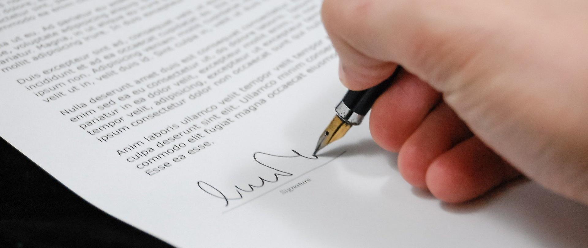 Zdjęcie przedstawia dłoń z długopisem w ręce piszącą po kartce