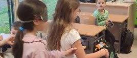 Dzieci uczą się prowadzić osobę niewidomą - korytarzem idą dwie dziewczynki, ta z opaską na oczach jest prowadzona przez koleżankę