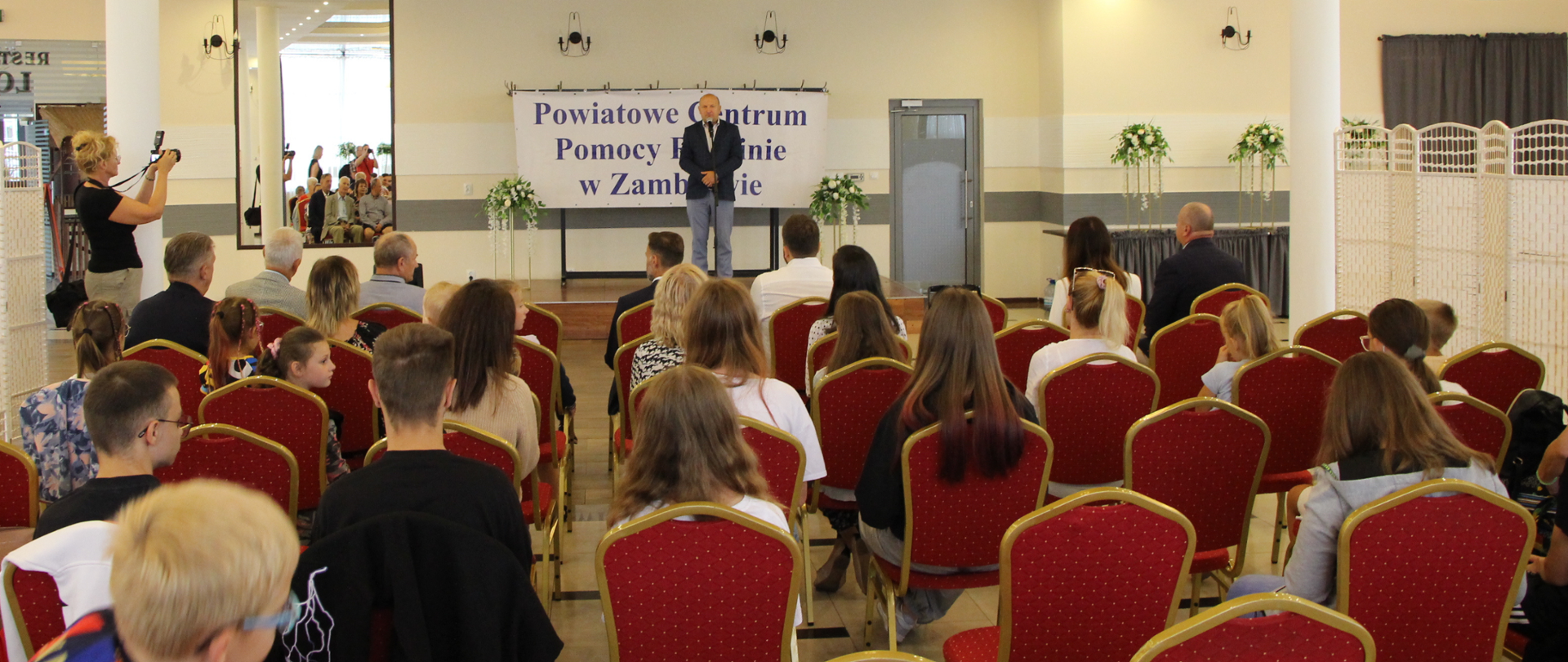 na zdjęciu w sali bankietowej Fabryki Jedzenia w Zambrowie, znajduje się widownia, a w tle kierownik PCPR, który przemawia podczas wydarzenia