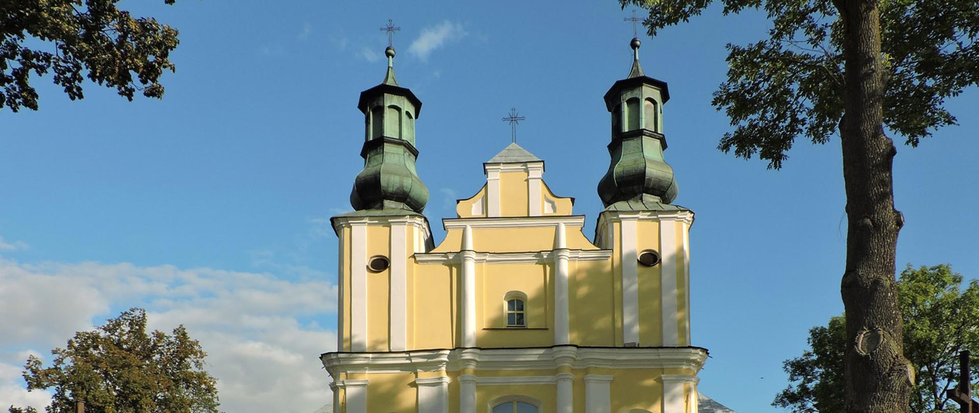 Zdjęcie przedstawia Kościół Świętego Jana Chrzciciela w Górznie. Jednonawowa budowla reprezentuje styl barokowy, jest orientowana, murowana, wzniesiona z cegły. Fasada jest ujęta z lewej i prawej strony dwiema czworobocznymi wieżami. Budynek jest żółto-biały. Wokół rosną drzewa.