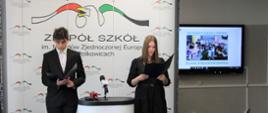 Na tle ścianki ekspozycyjnej z logo Zespołu Szkół im. Narodów Zjednoczonej Europy stoją elegancko ubrani uczniowie. Pomiędzy nimi stoi stolik z mikrofonami.
