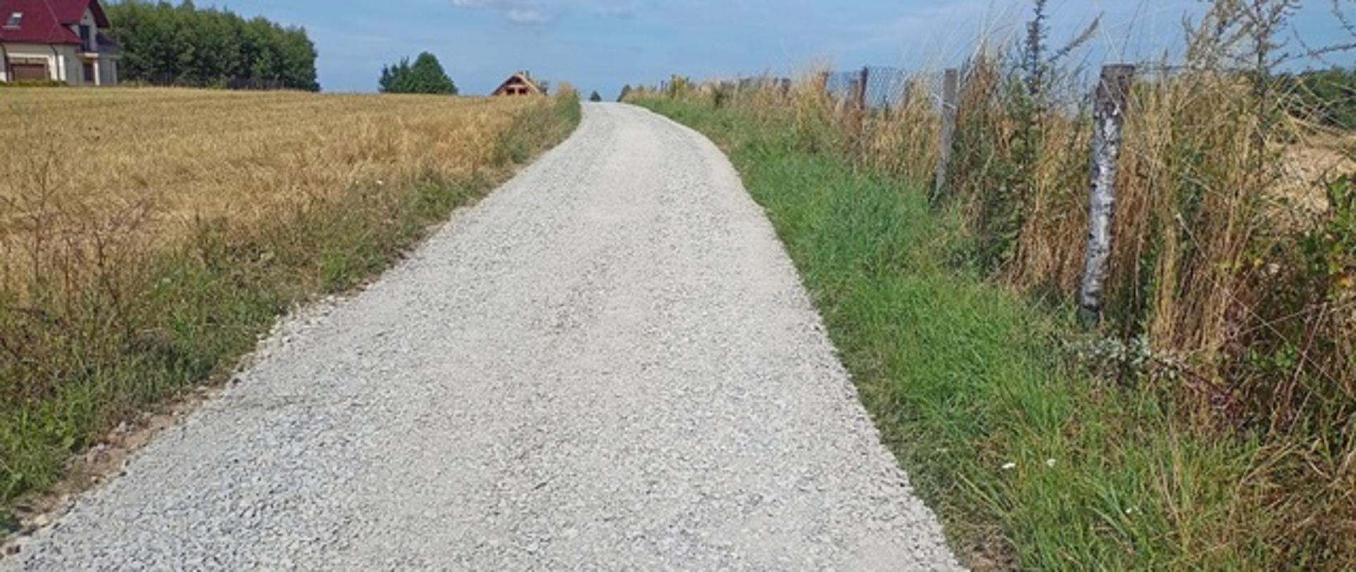 droga kamienna po lewej i po prawej stronie drogi widoczne pola uprawne a w oddali fragmenty domów