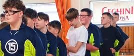 Młodzi zawodnicy ze szkoły w strojach granatowo-zielonych stoją w rzędzie jeden za drugim