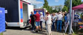 Festyn Profilaktyczno Zdrowotny w ogrodach przasnyskiego szpitala. Zdjęcie przedstawia osoby oczekujące w kolejce do wykonania badania skóry i znamion w Dermatobusie.