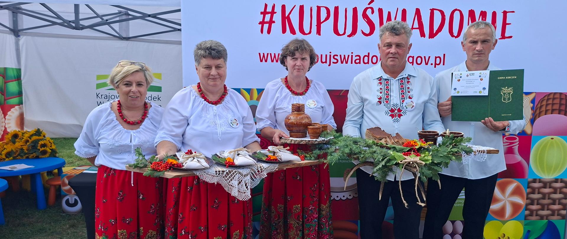 trzy kobiety i dwóch mężczyzn. Dwie kobiety i jeden mężczyzna trzymają w rękach tace z jedzeniem. W tle duży napis: KUPUJŚWIADOMIE