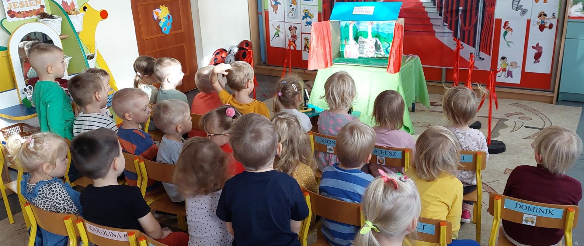 Dzieci siedzą na krzesełkach , przed nimi teatrzyk