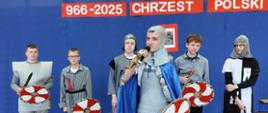 Chłopcy przebrani za rycerzy z mieczami i tarczami, na przodzie uczeń przebrany za Mieszka I przemawia do mikrofonu