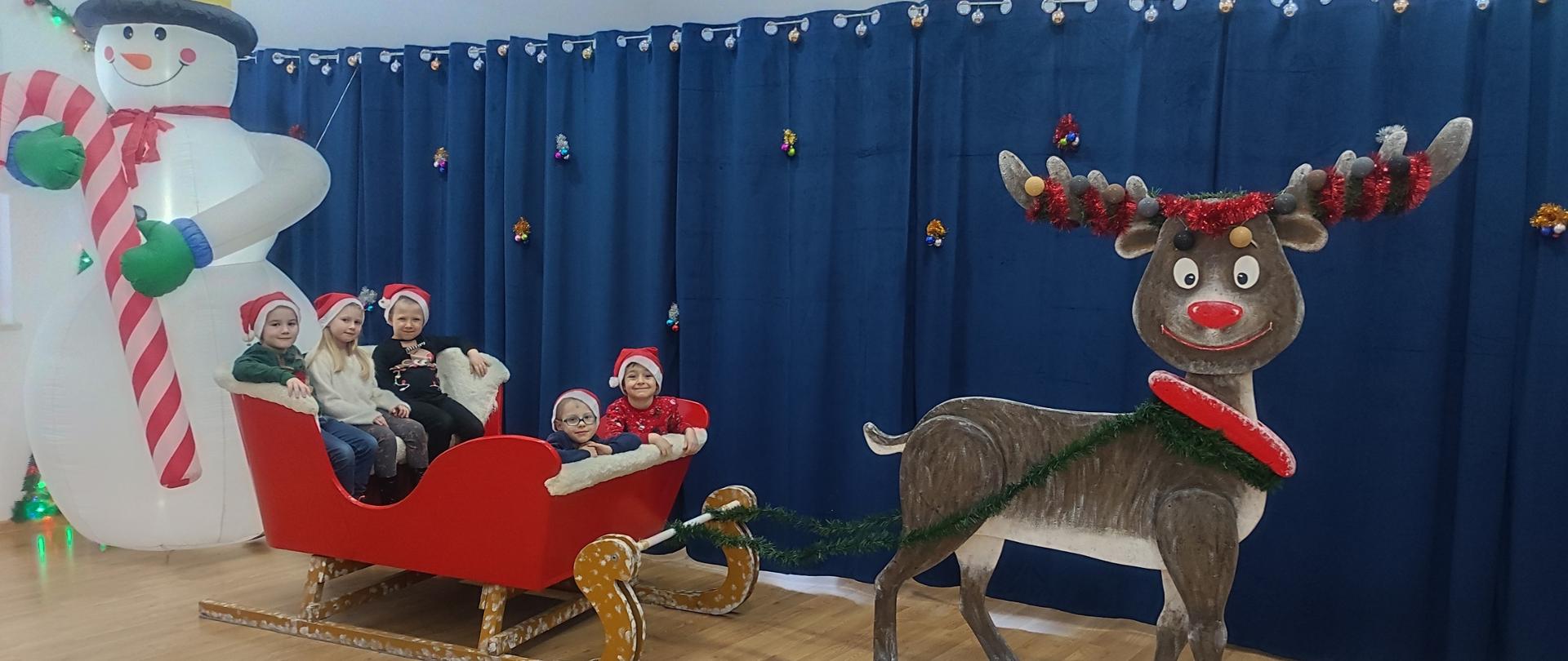 Dzieci w saniach z reniferem , za nimi bałwan 