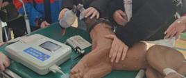 3 uczennice i 1 uczeń z klasy 8 stoją przy noszach, przy których przeprowadzają dotlenianie przez maskę źrebaka, podłączonego do urządzenia EKG, źrebak wykonany jest z tworzywa sztucznego