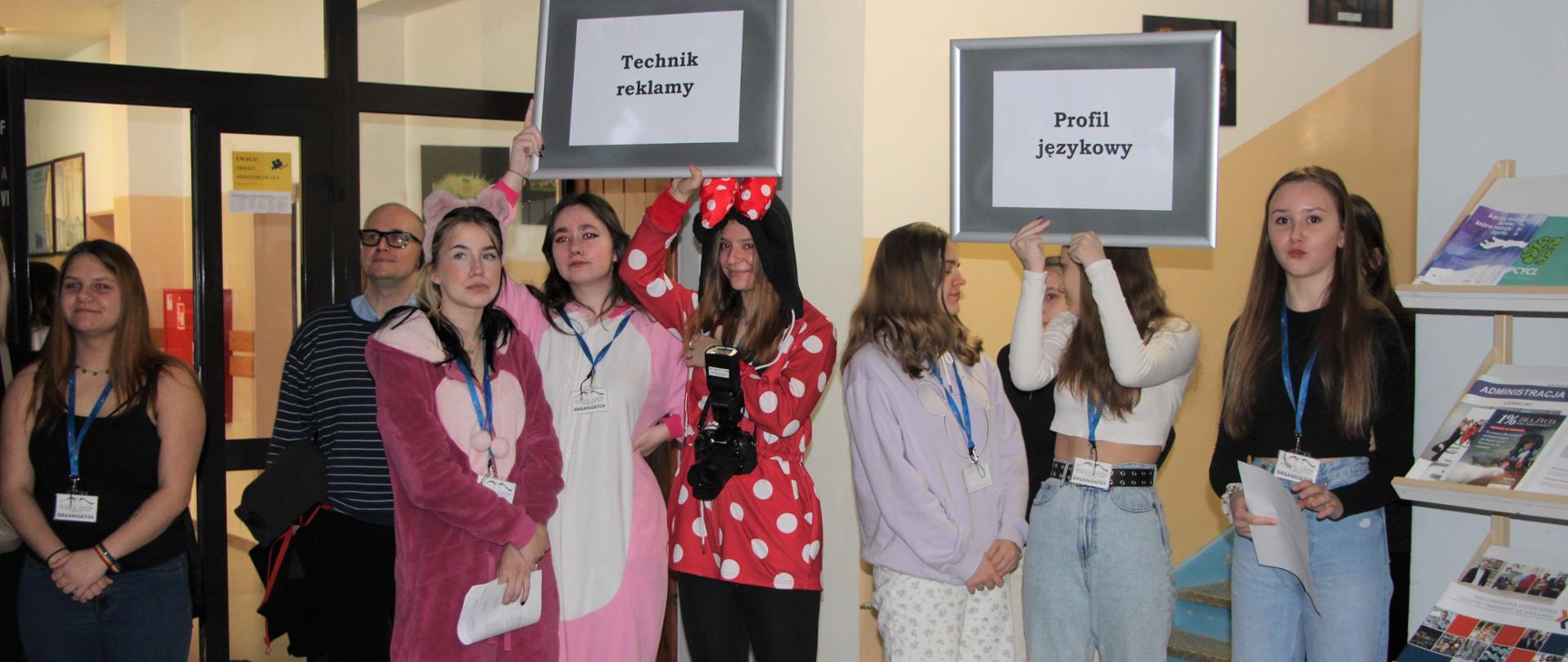 Uczniowie stoją na korytarzu w kolorowych strojach i trzymają w rękach tablice z napisami
