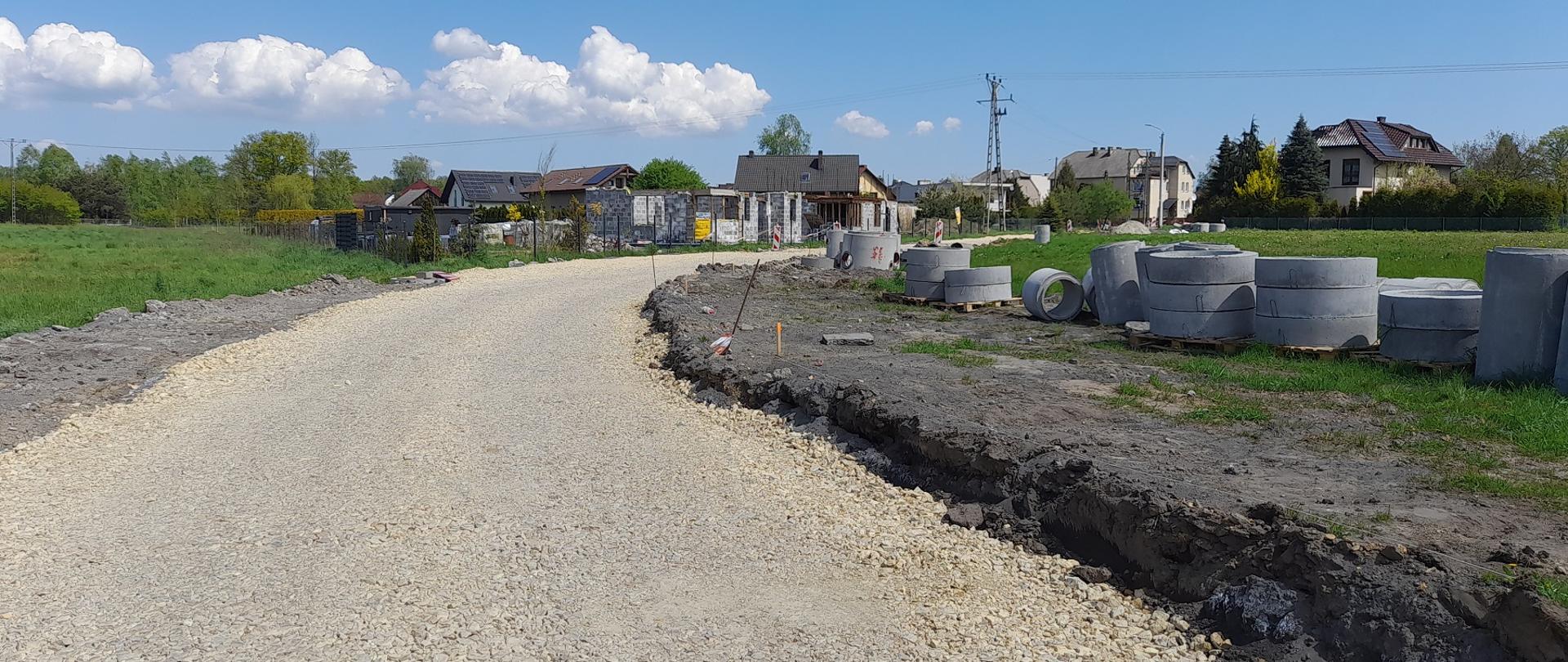 Kamienna podbudowa drogi gminnej obok rury kanalizacyjne a w tle zabudowania mieszkalne
