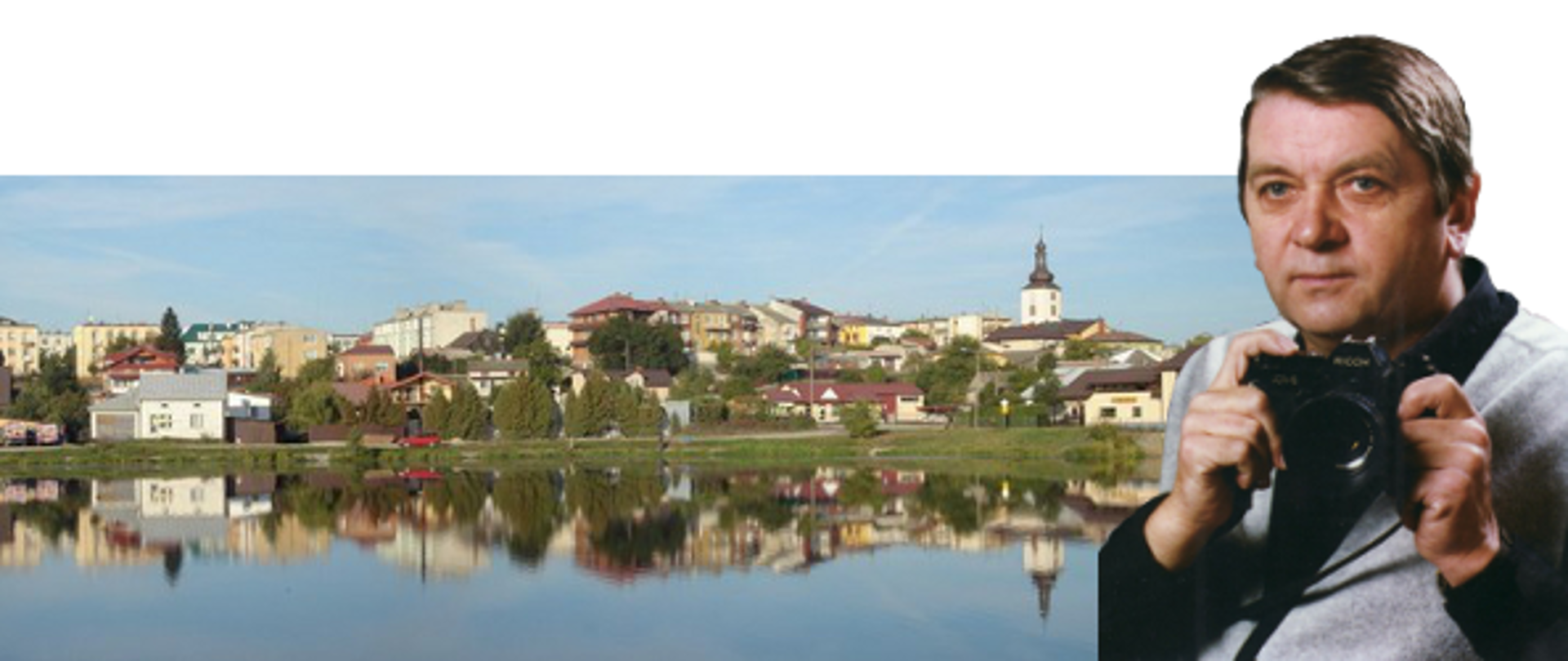 Zdjęcie przedstawia Pana Jana Skrzypczyńskiego trzymającego w rękach aparat fotograficzny na tle panoramy miasta od strony zalewu.