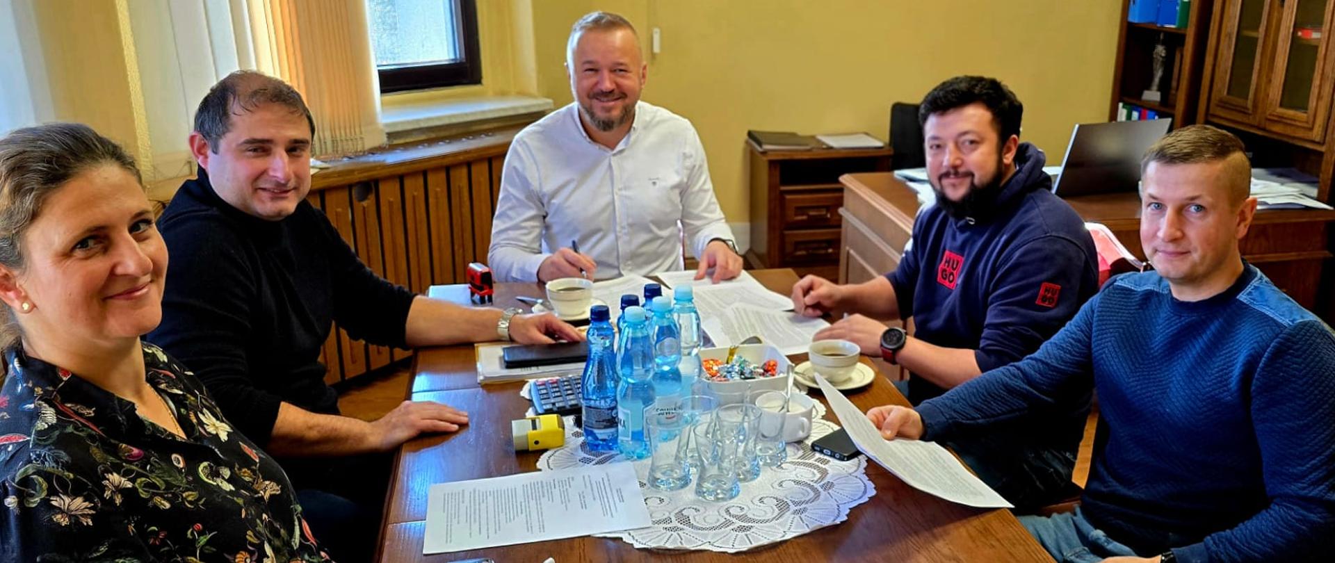 Pięć osób siedzi w biurze przy drewnianym stole z dokumentami.