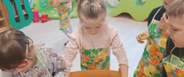 Wspólne pieczenie pierniczków - dzieci siedzą przy stole i wykonują czynności związane z przygotowaniem ciasteczek. Pozują przy tym do zdjęć