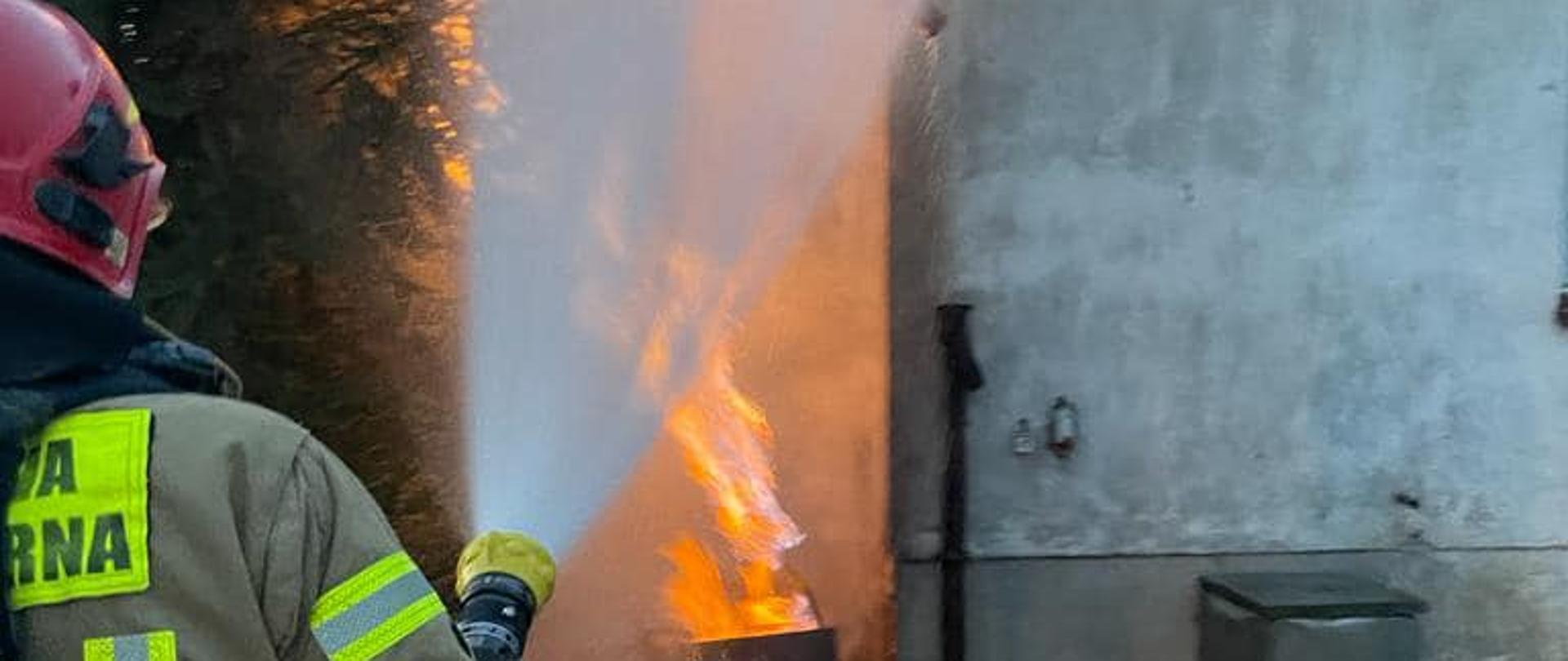 Strażak w czerwonym hełmie gaszący pożar