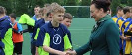 Drużyna piłkarzy w granatowo-seledynowych koszulkach odbiera gratulacje od pani wójt Gminy Łabowa, pani wójt ściska rękę pierwszego zawodnika 