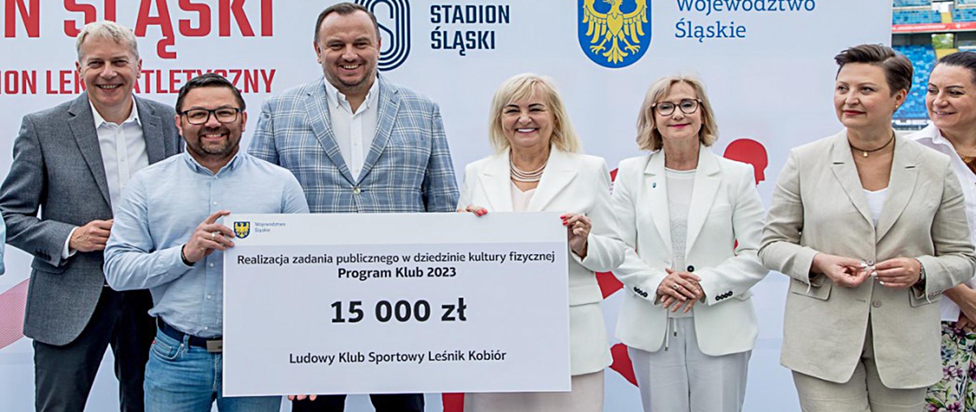 Grupa osób trzymająca symboliczny czek na kwotę 15 tyś. zł. przekazany prezesowi Leśnika Kobiór za wzięcie udziału w programie Klub 2023.