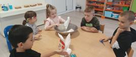 Wspólne pieczenie pierniczków - dzieci siedzą przy stole i wykonują czynności związane z przygotowaniem ciasteczek. Pozują przy tym do zdjęć