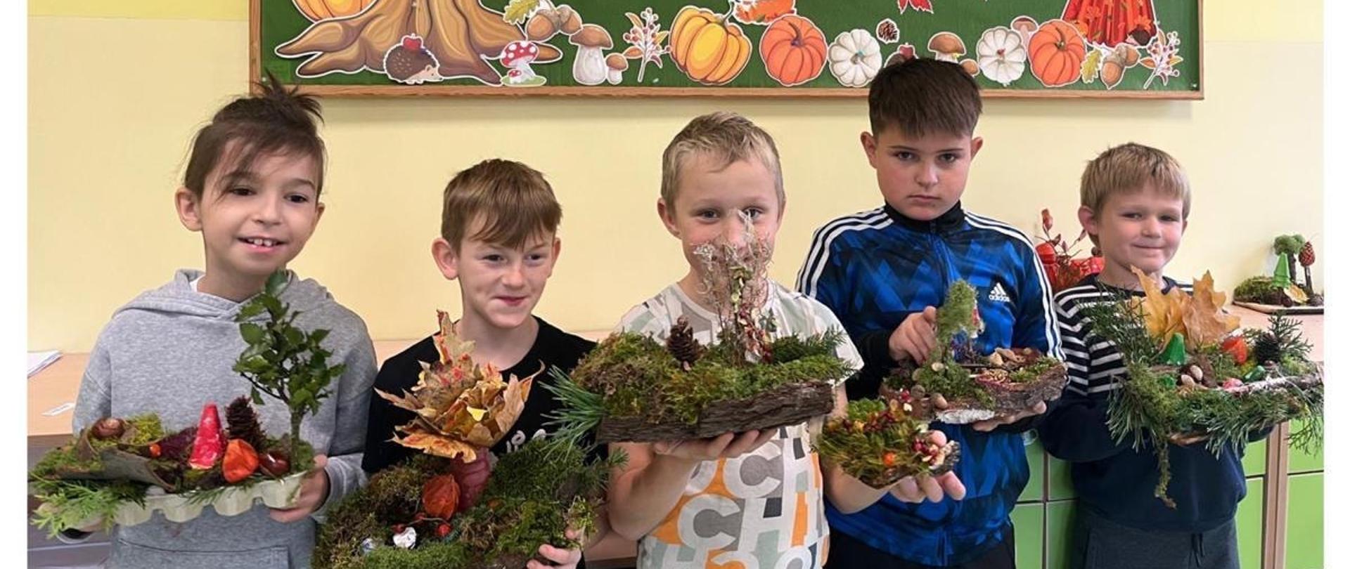 Zdjęcie podzielone na 2 okna, górne okno przedstawia uczniów trzymających w rękach prace przestrzenne wykonane z naturalnych leśnych darów przedstawiające las, dolne okno przedstawia uczennice trzymające swoje prace