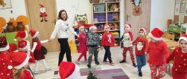 Dzieci ubrane na czerwono, w czapkach świętego Mikołaja tańczą w kółku