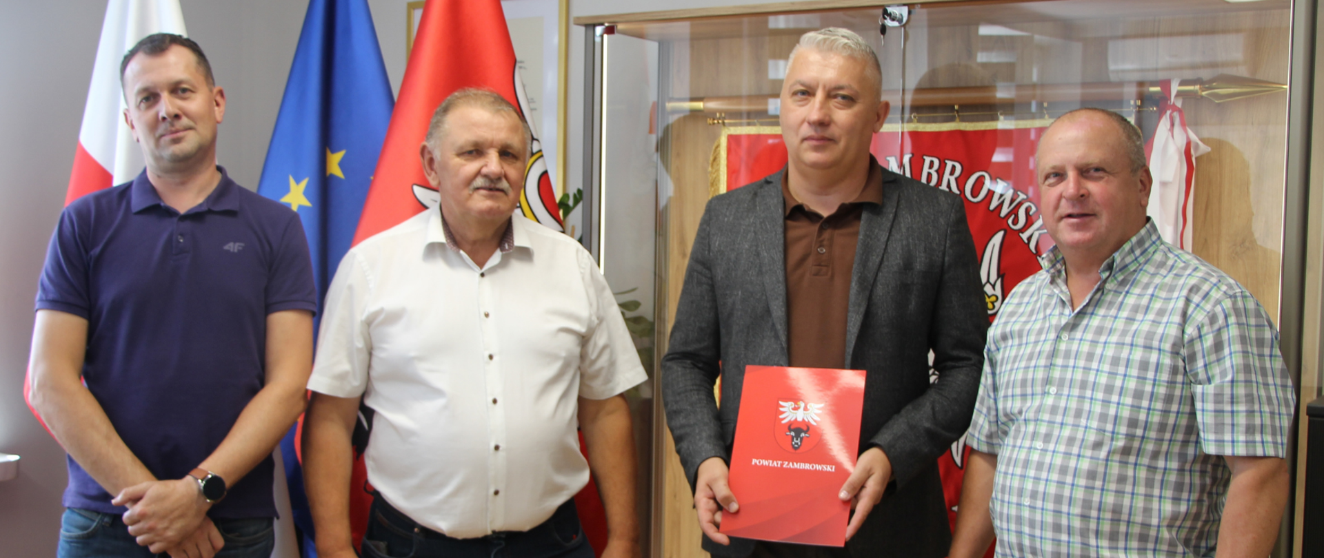 Od lewej zastępca naczelnika wydziału IR, członek zarządu Powiatu Zambrowskiego Krzysztof Wasiulewski, przedstawiciel wykonawcy firmy BIK Projekt z Łomży oraz wicestarosta zambrowski pozują do zdjęcia, podczas gdy wykonawca trzyma w rękach umowę na kompleksową modernizację trasy Kołaki Kościelne – Łętowo-Dąb