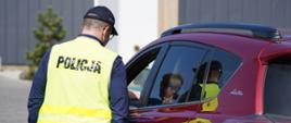 Policjant w żółtej kamizelce z czarnym napisem Policja stoi przed samochodem.