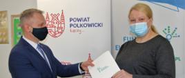 Mężczyzna wręcza kobiecie biało niebieską teczkę z symbolicznym projektem Akademia Niezależnego Życia.