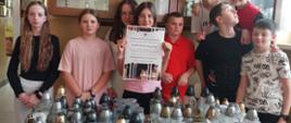 Uczniowie stoją przy zebranych zniczach, dziewczynka na środku trzyma w ręku plakat Szkolnego Kola Wolontariatu promujący akcję "Światełko dla tych, którzy odeszli" 