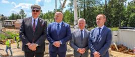 Na zdjęciu uczestnicy spotkania z dziennikarzami pozują do zdjęcia na tle prac budowlanych.`