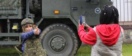 Dziewczynka w akcesoriach wojskowych pozuje do zdjęcia na tle pojazdu wojskowego