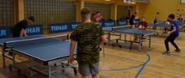 W trakcie turnieju - uczestnicy stoją przy stołach, rozgrywają rundy tenisa