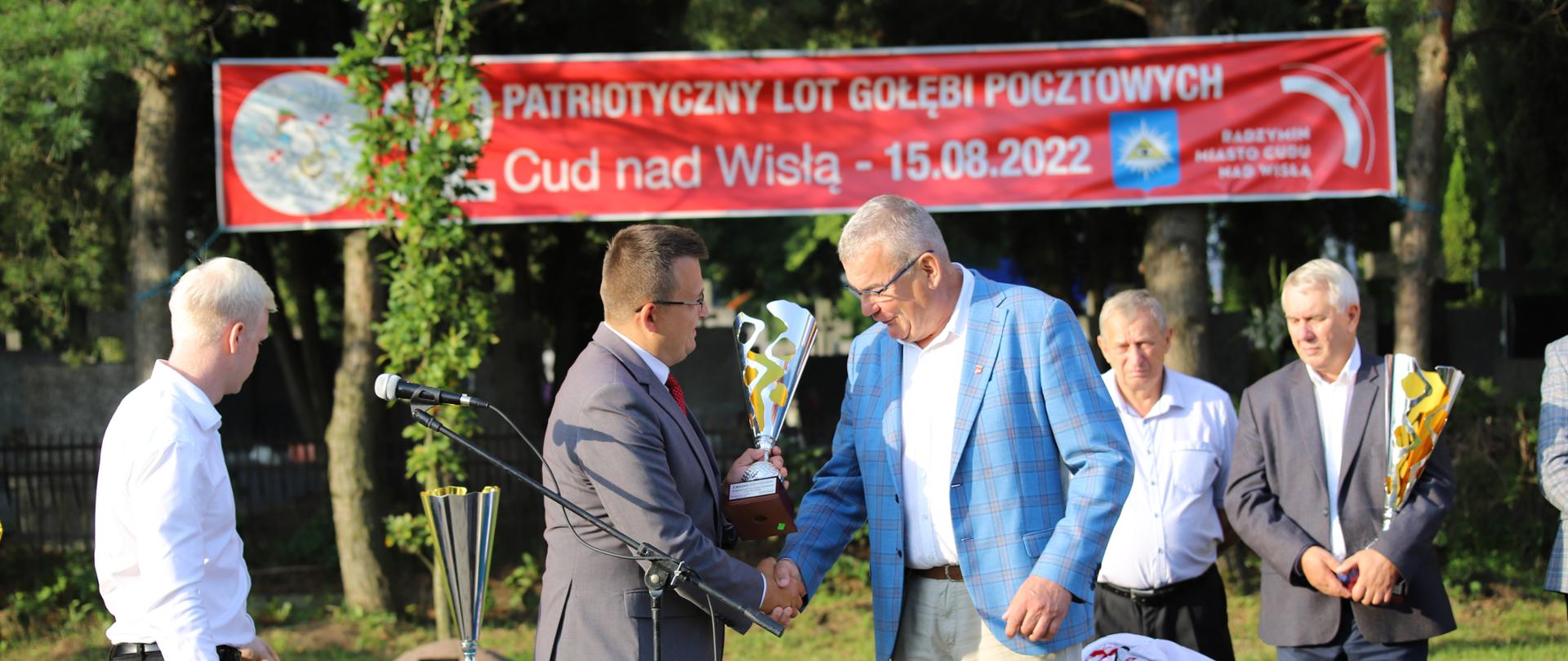 Mężczyźni ściskają sobie dłoń i przekazują puchar 