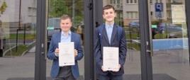 Przed wejściem głównym Akademii Nauk Stosowanych w Nowym Sączu stoją dwaj uczniowie ubrani odświętnie z dyplomami