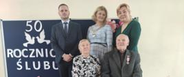 Państwo Agnieszka i Edward na tle granatowej tablicy z napisem wraz z Wójtem, Z-cą Wójta i Z-cą Kierownika USC