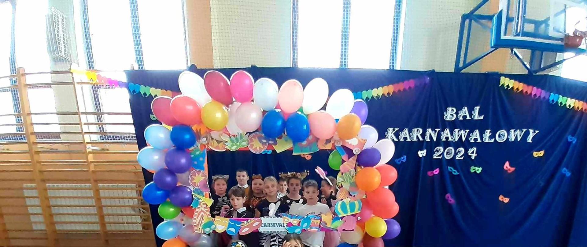 Uczniowie w strojach karnawałowych na tle dekoracji z napisem "Bal Karnawałowy 2023"