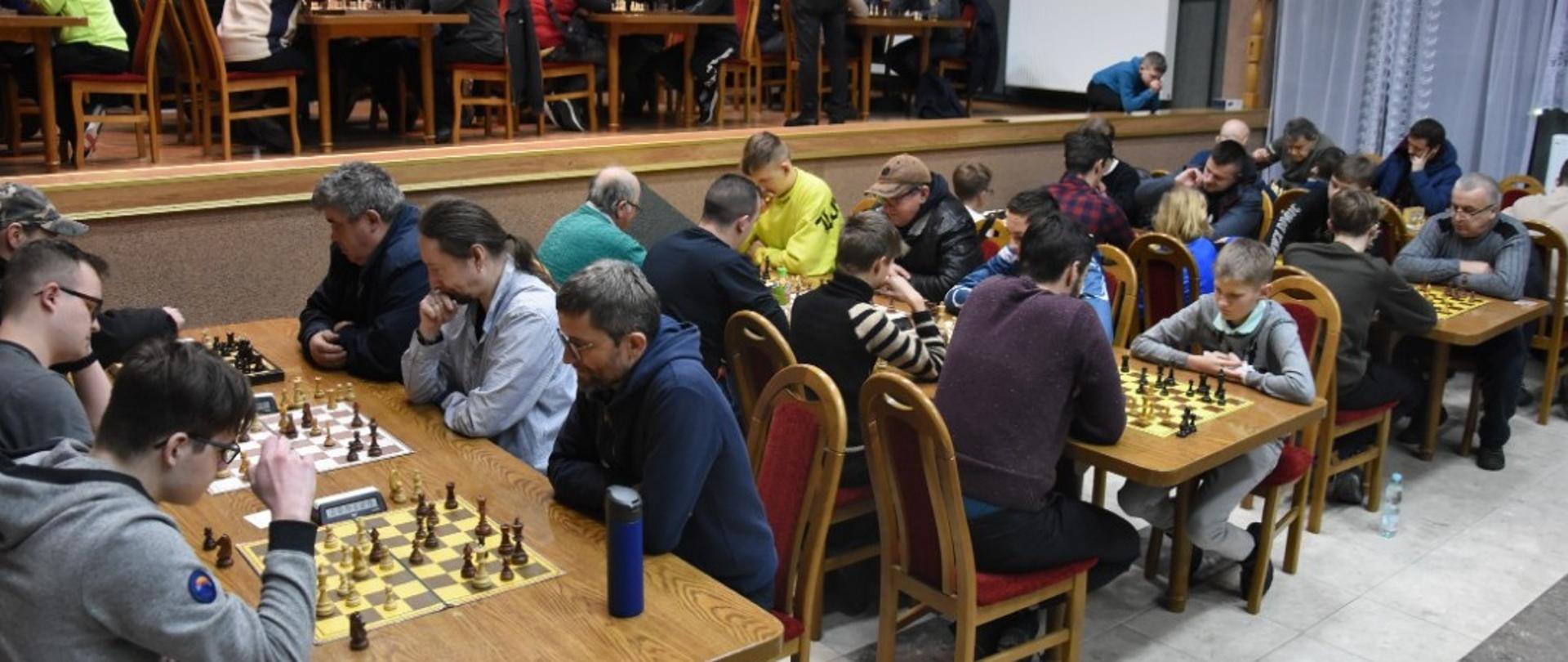 Na zdjęciu szachiści siedzący przy stolikach w trakcie turnieju