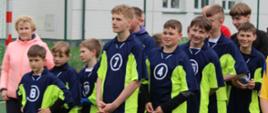 Drużyna piłkarzy w granatowo-seledynowych koszulkach wraz z nauczycielem wychowania fizycznego stoi na boisku przy szkole podstawowej w Łabowej