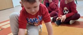 Dzieci siedzą na dywanie, mają przed sobą karty - będące częścią gry edukacyjnej