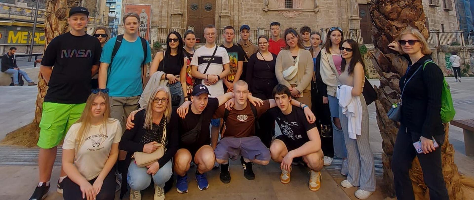 Grupa uczniów wraz z opiekunami pozuje do wspólnego zdjęcia przy palmach