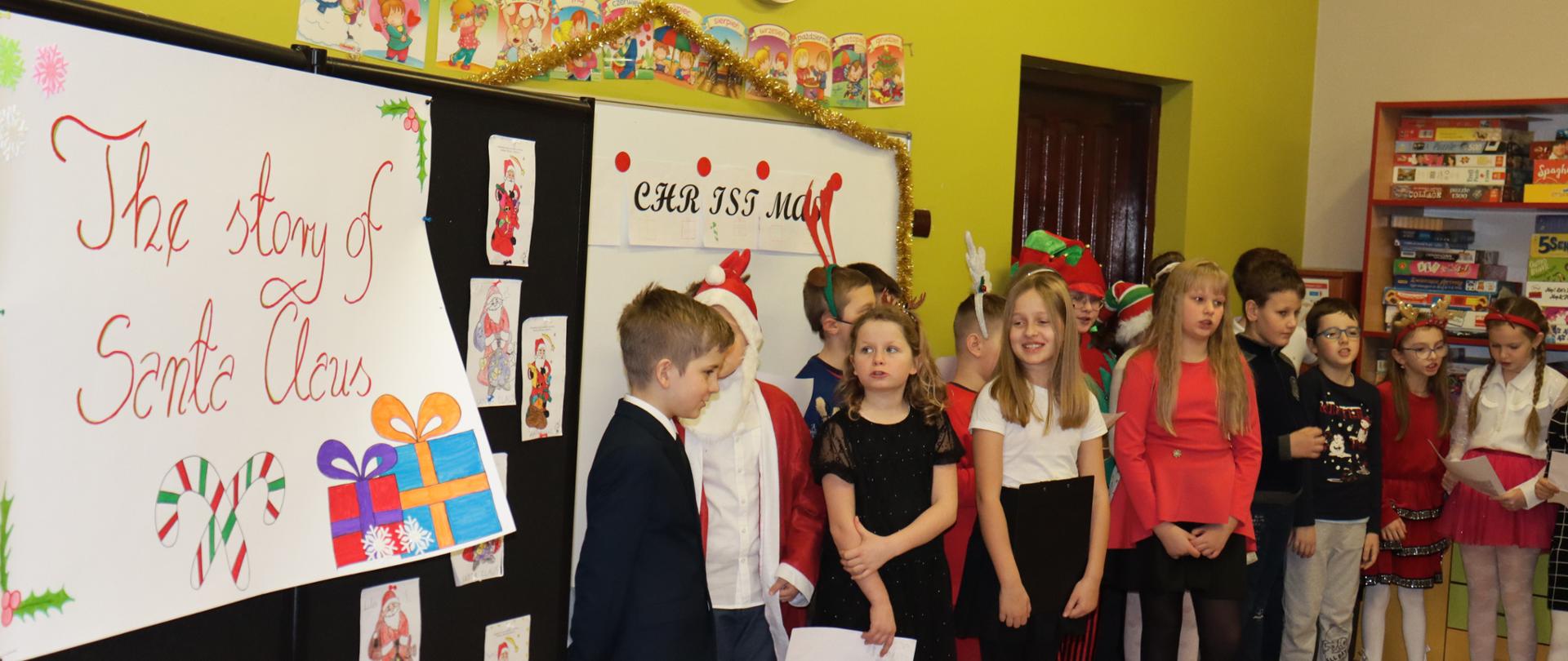 Wszyscy aktorzy stoją i śpiewają piosenkę, po lewej tablica z napisem The story of santa claus