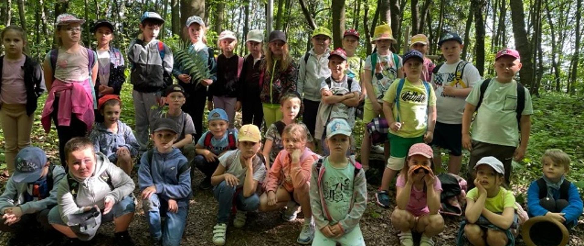 Na zdjęciu widać grupę dzieci w lesie.