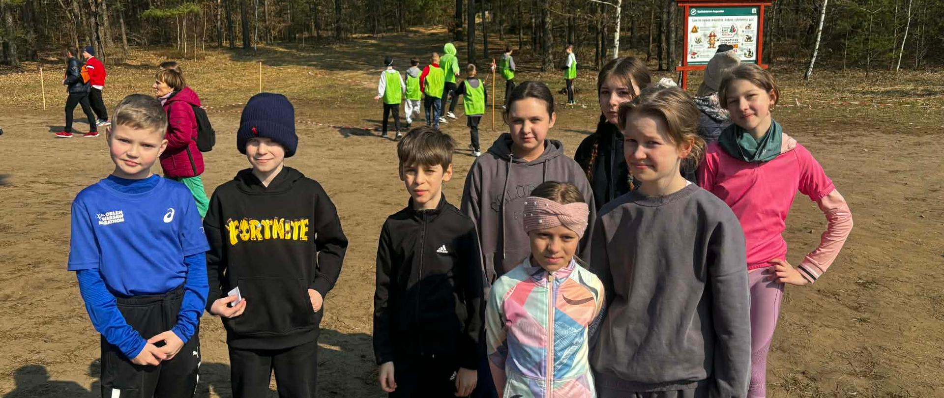 Ośmioro uczniów reprezentujących naszą szkołę w biegach przełajowych pozuje do wspólnego zdjęcia.