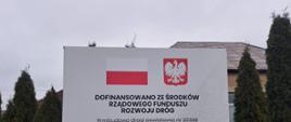 na zdjęciu znajduje się tablica z informacją o dofinansowaniu ze środków Rządowego Funduszu Rozwoju Dróg "Przebudowa drogi powiatowej nr 2036B Paproć Duża - granica województwa" dofinansowanie 2 585 566,42 zł, całkowita wartość 5 171 132,85 zł, data podpisania umowy lipiec 2025