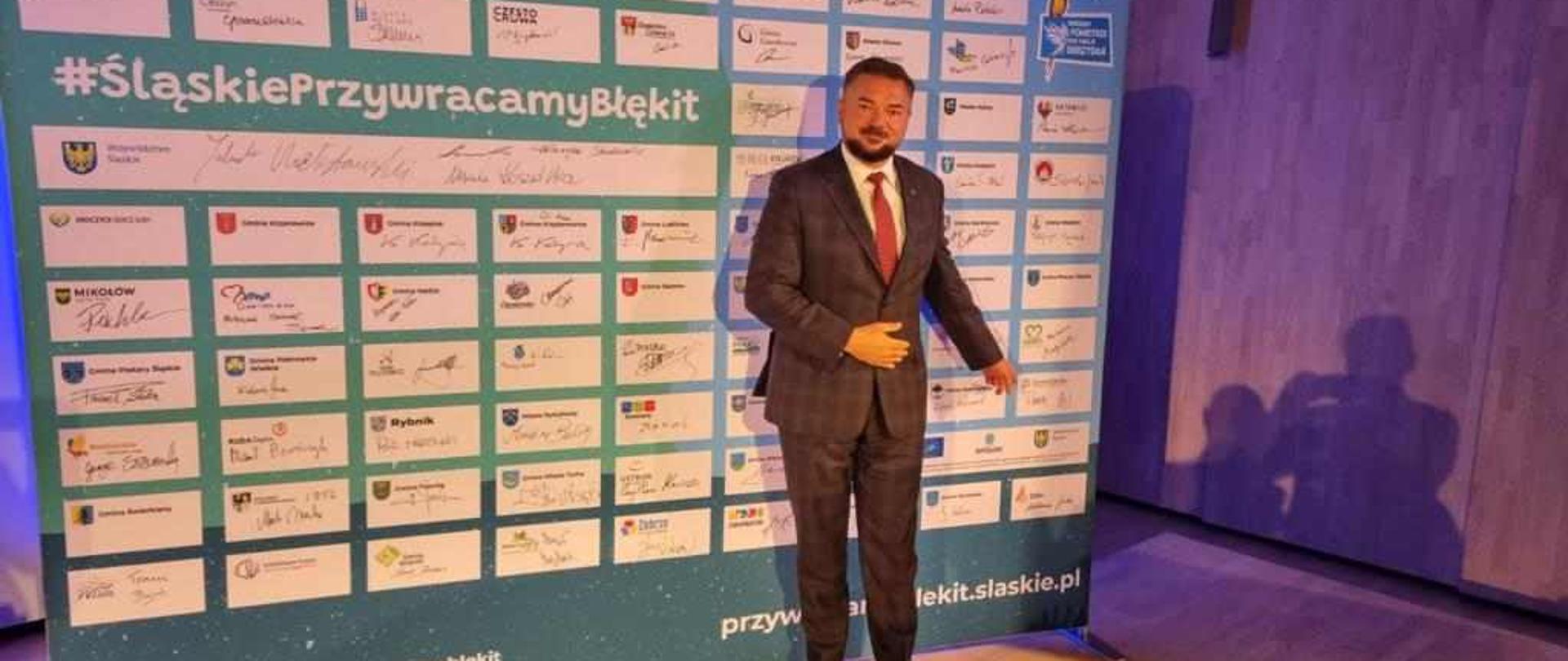 Marek Cyl na tle ścianki, na której chwilę temu złożył zwój podpis