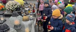 Grupa dzieci na cmentarzu zapala znicze w nawiązaniu do Święta Zmarłych