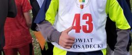 Uczeń w koszulce z numerem 43 i napisem "Powiat nowosądecki" unosi rękę z wyciągniętym do góry kciukiem, w tle widoczni inni uczestnicy biegów