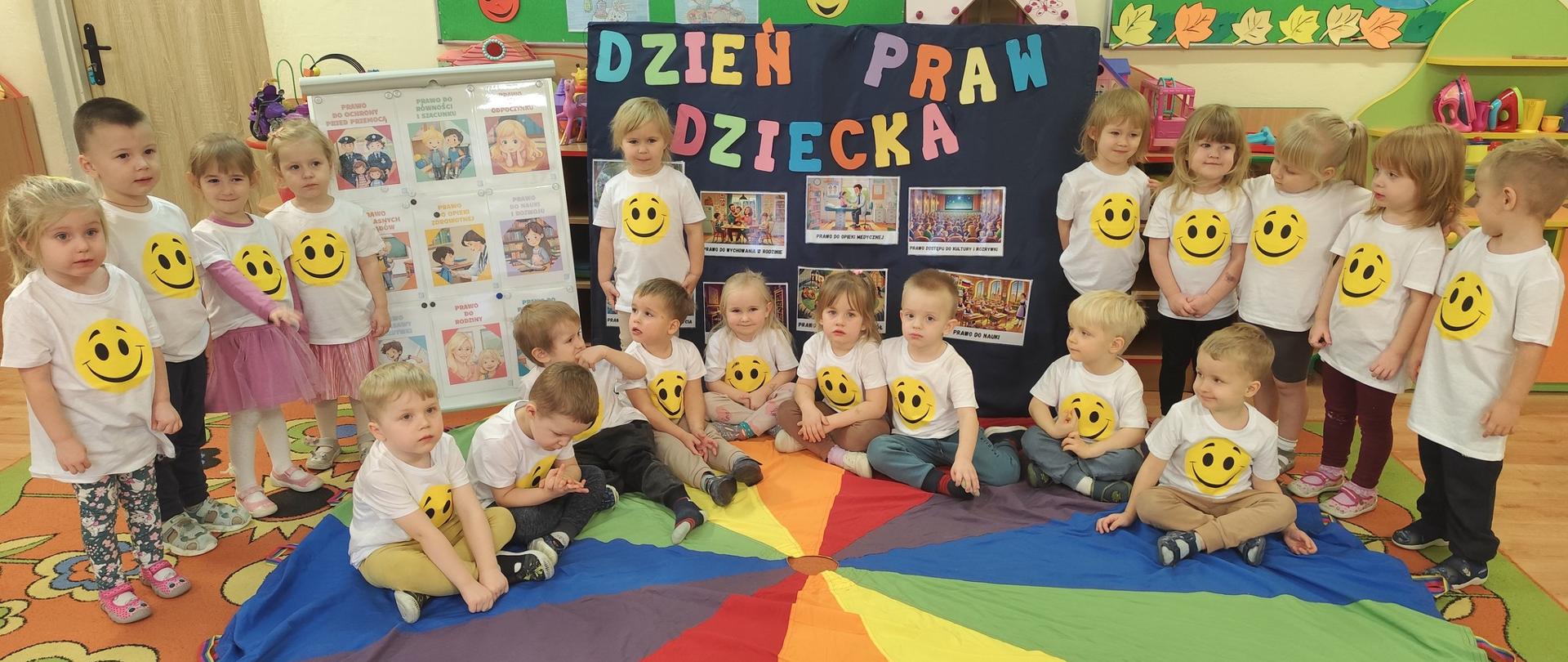 Grupa dzieci w białych koszulkach na tle napisu DZIEŃ PRAW DZIECKA