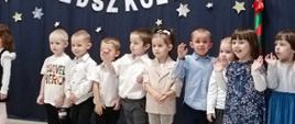 Przedszkolaki stoją w sali na tle ścianki "Pasowanie na przedszkolaka"
