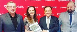Na zdjęciu od lewej stoją: Wójt Gminy Pokrzywnica Adam Dariusz Rachuba, Skarbnik Gminy Magdalena Lusa trzymająca dokument oraz Marszałek Województwa Mazowieckiego Adam Struzik. W tle widoczny jest czerwony baner z napisem „Mazowsze”.
