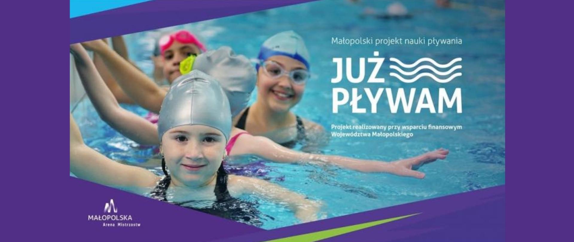 Grupa uśmiechniętych dzieci w czepkach i okularach pływackich stoi w basenie, machając do kamery. Tło wypełnia błękitna woda krytej pływalni. Baner promuje małopolski projekt edukacyjny „Już pływam”, realizowany przy wsparciu finansowym Województwa Małopolskiego. Widoczne są logotypy i hasła związane z inicjatywą „Małopolska Arena Młodych”.